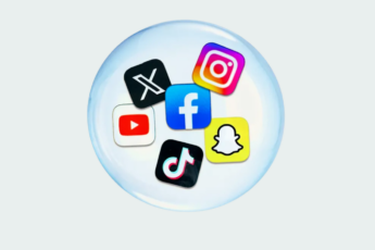 Six colorful social media platform icons arranged in a circular pattern within a translucent glass sphere: X (formerly Twitter) with a white X on black background in the top left, Instagram with its gradient logo in the top right, Facebook with its blue logo in the center, YouTube with a red play button on white background on the left, TikTok with a pink and white musical note on black background at the bottom, and Snapchat with a yellow ghost icon on the bottom right. The sphere sits on a light gray background with a subtle shadow effect.