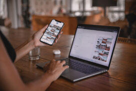 Woman edits social media content on phone and laptop at a cafe