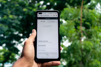 A hand holding a smartphone displaying the ChatGPT app open on chat.openai.com, with GPT-3.5 and GPT-4 tabs visible, against a blurred green tree background.